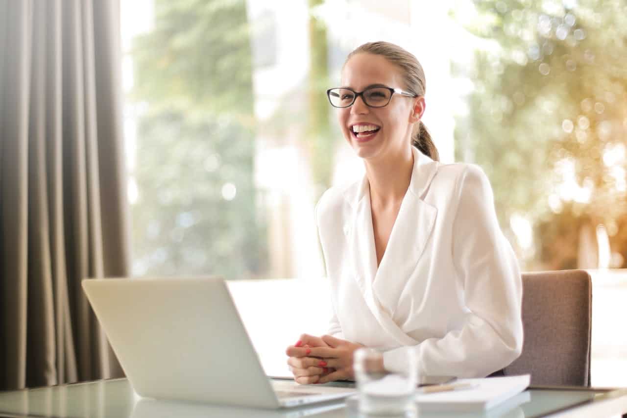 services-bg Cheerful businesswoman in glasses working on a laptop, in a bright and modern office setting.